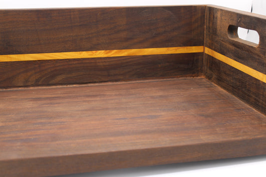 A close-up of a dark brown wooden serving tray with a lighter yellow wood inlay stripe and a cutout handle on the side.