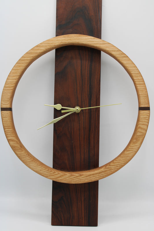 A minimalist wall clock featuring a light oak circular frame and a dark brown wood-grain vertical rectangular base, with slim gold-toned hands.