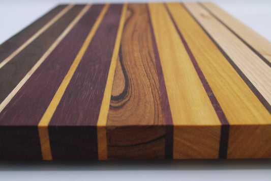Wooden cutting board with gradient colors ranging from dark brown to purple to medium brown to yellow to light brown.