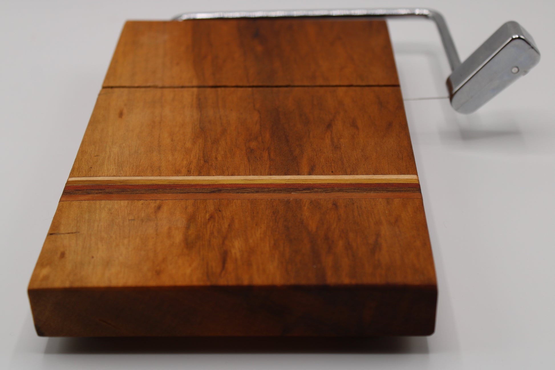 Wooden cheese cutting board with slicer on a light gray background