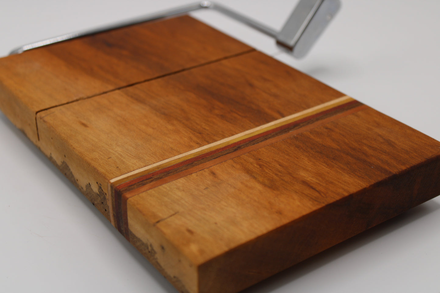 Wooden cheese cutting board with slicer on a light gray background