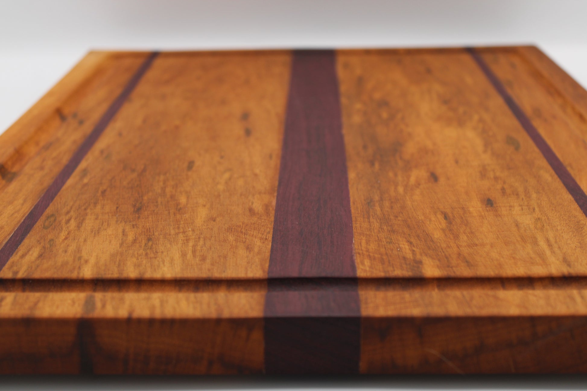 Wooden cutting board with purpleheart inlay on a white background