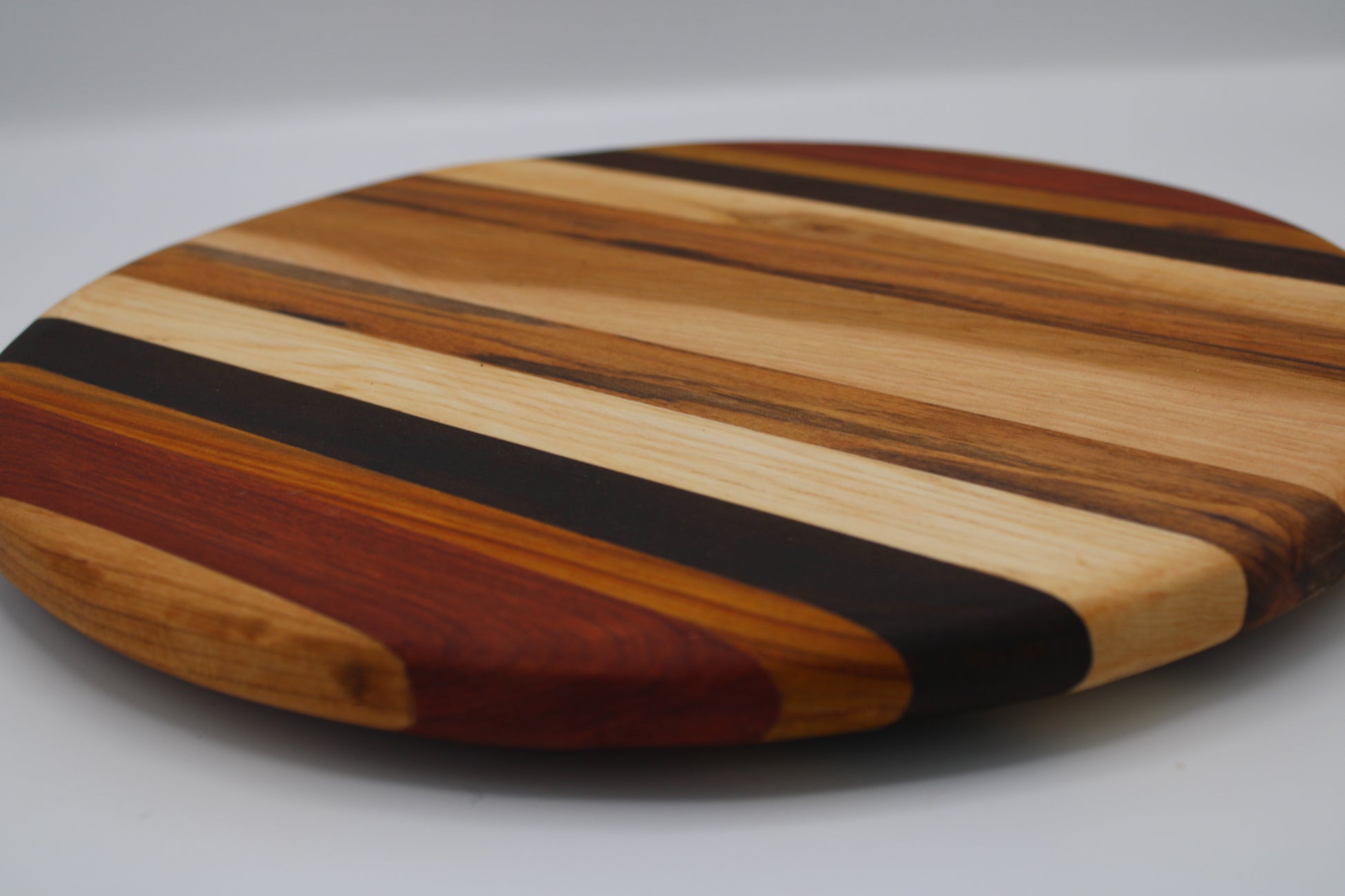 Round wooden cutting board with striped pattern on a gray background