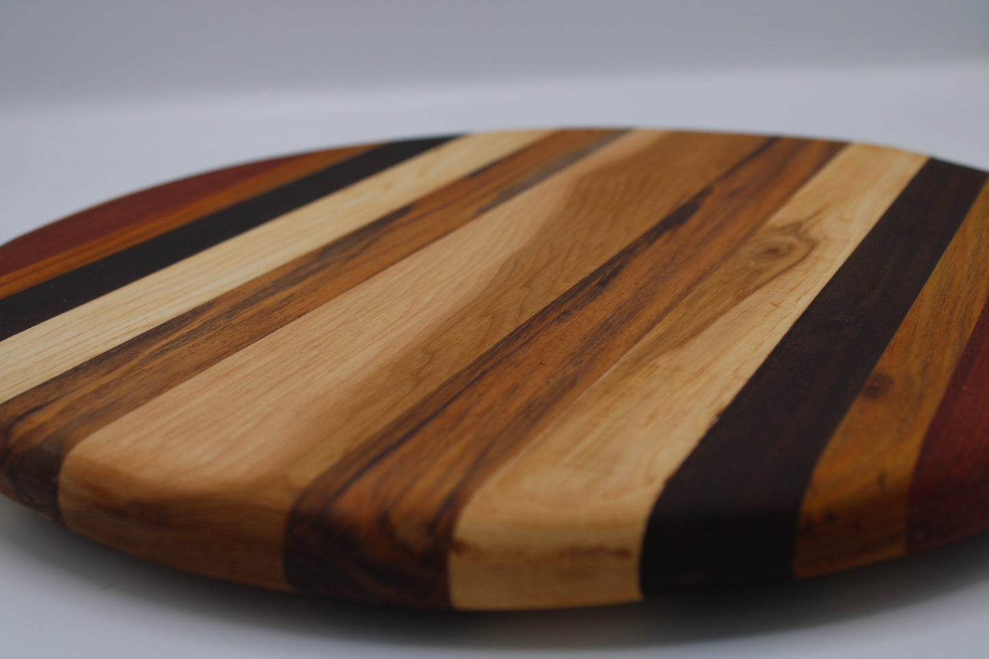 Round wooden cutting board with striped pattern on a gray background