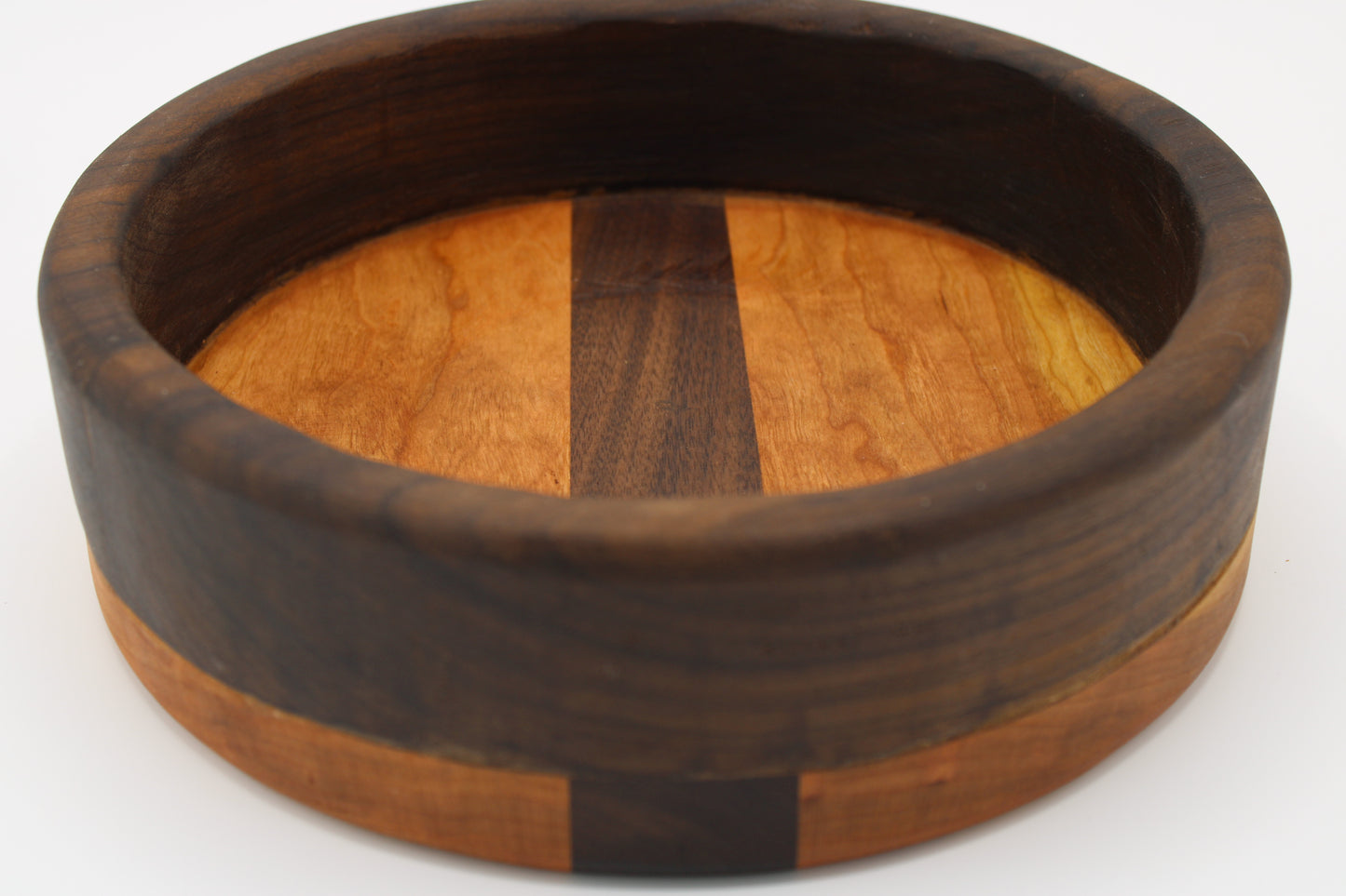 A round wooden bowl with a thick dark brown outer rim and a lighter warm brown inner band, featuring a vertical dark wood stripe down the center, shown on a white background.