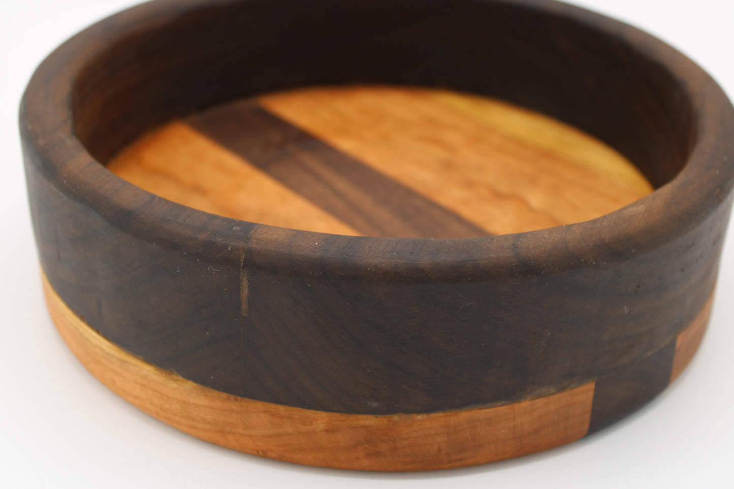 A round wooden bowl with a dark brown outer band and a lighter natural wood interior featuring diagonal stripes.