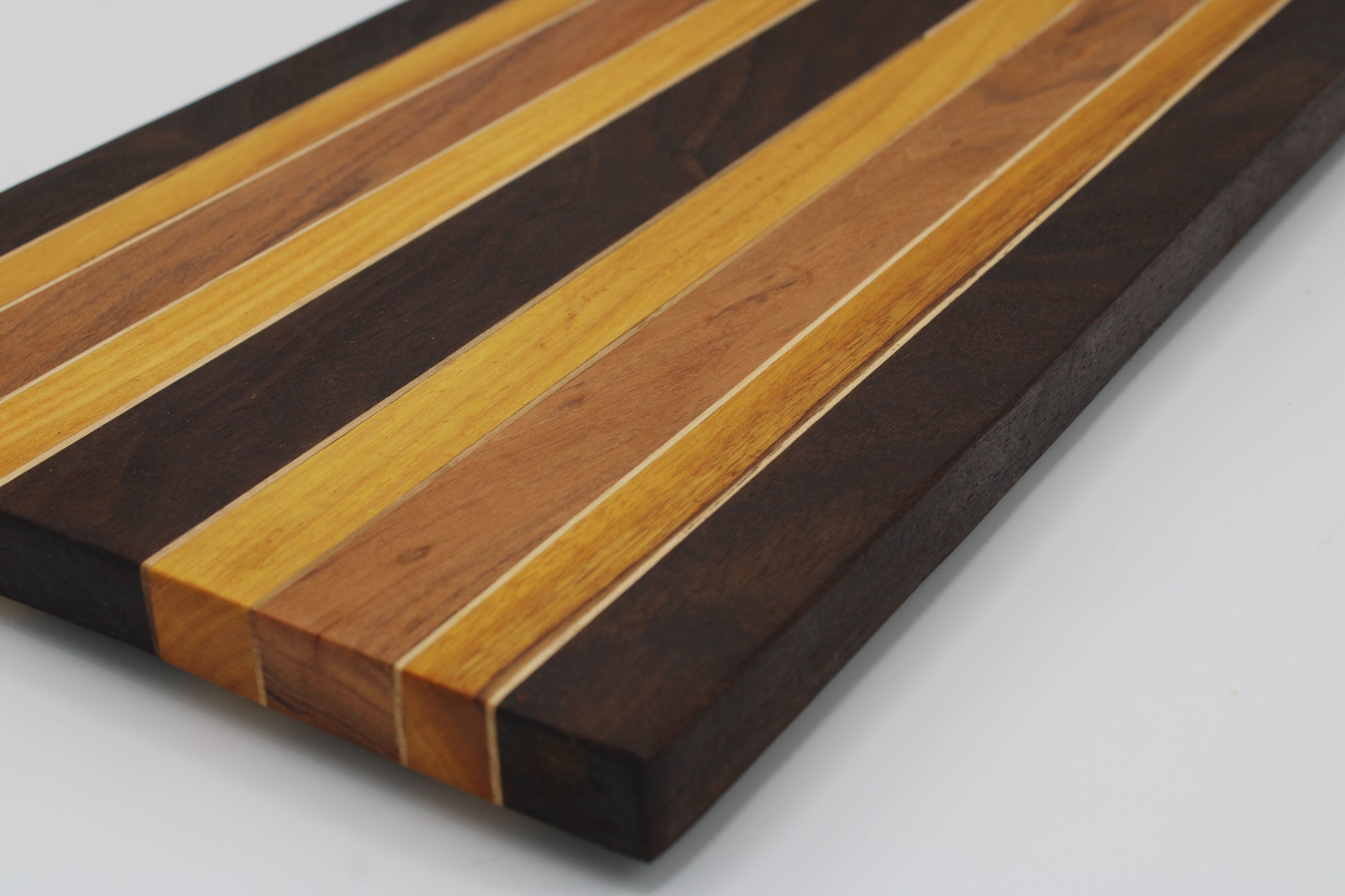 A rectangular wooden cutting board with a striped inlay pattern of alternating light honey, medium brown, and dark espresso wood tones, shown on a plain white background.