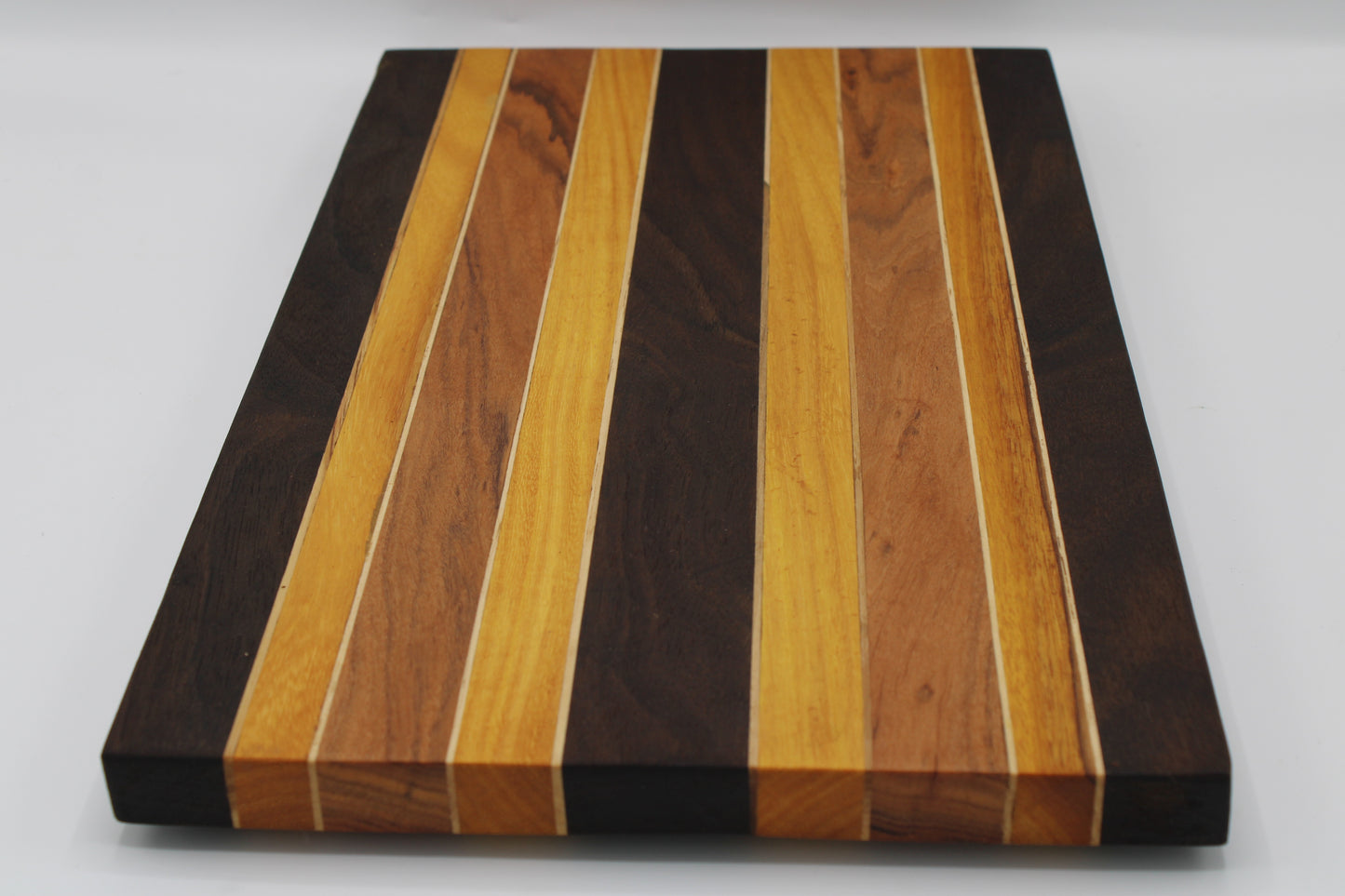 A rectangular wooden cutting board with a striped pattern of alternating light and dark wood grain inlays, shown on a plain light gray background.