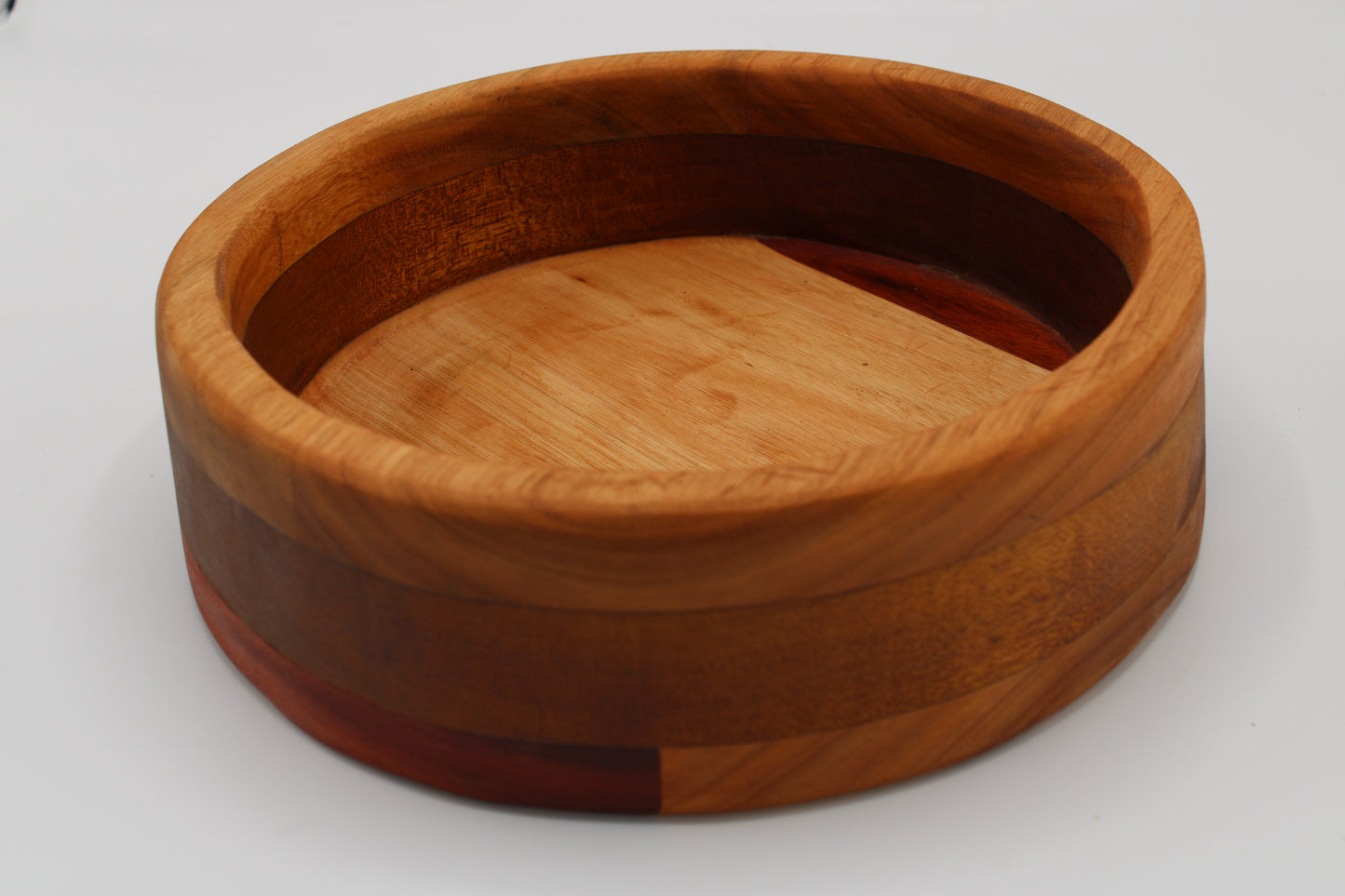 A round wooden bowl with a multi-layered wood grain pattern, featuring a light tan center and darker reddish-brown outer rings, photographed on a neutral light gray background.