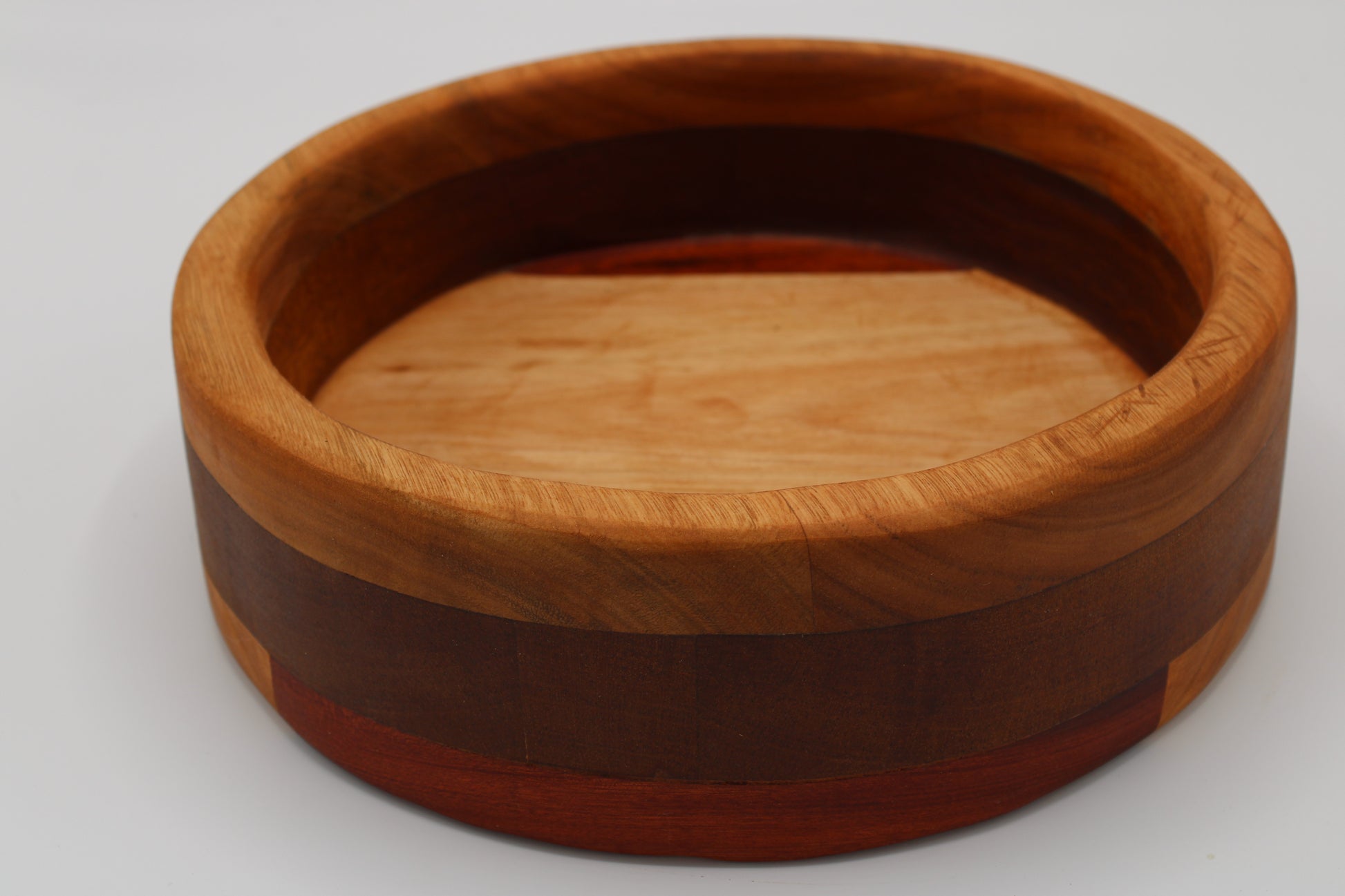 A round wooden bowl with a layered inlay design, featuring a light tan cherry wood top, a dark reddish-brown middle band, and a reddish-brown outer band, shown on a light gray background.