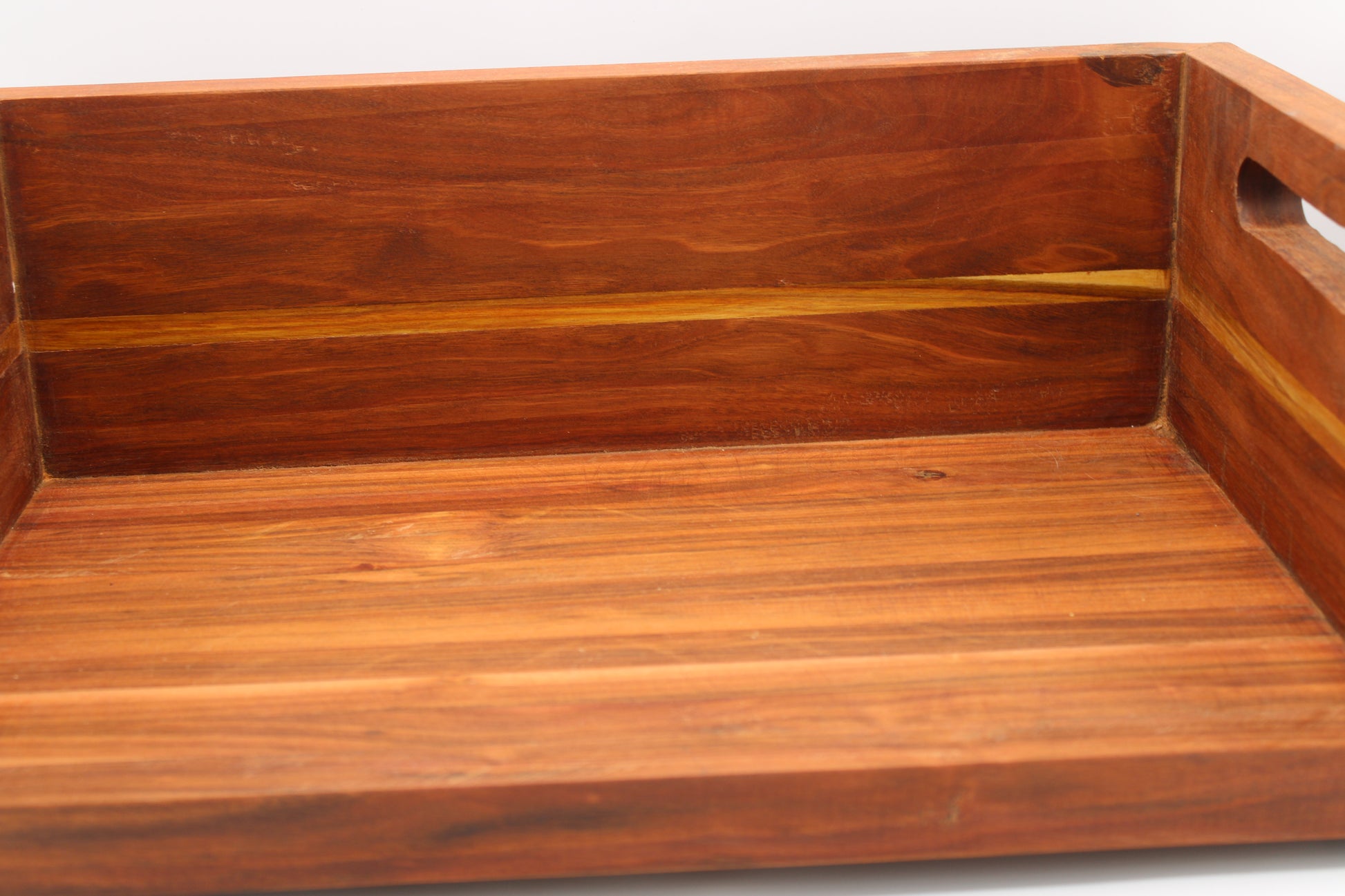 A close-up of a rectangular wooden serving tray with a warm reddish-brown finish and visible wood grain, showing the interior and side cutout handle against a plain white background.