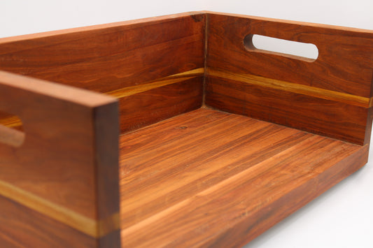 A close-up of a rectangular wooden serving tray with a warm reddish-brown finish and lighter wood inlay accents, featuring cutout handles on two sides.