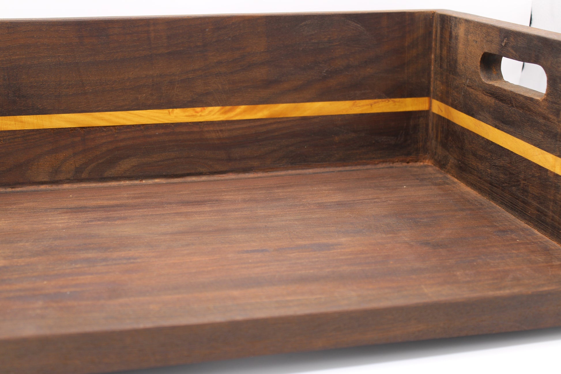 A close-up of a dark brown wooden serving tray with a lighter yellow wood inlay stripe and a cutout handle on the side.