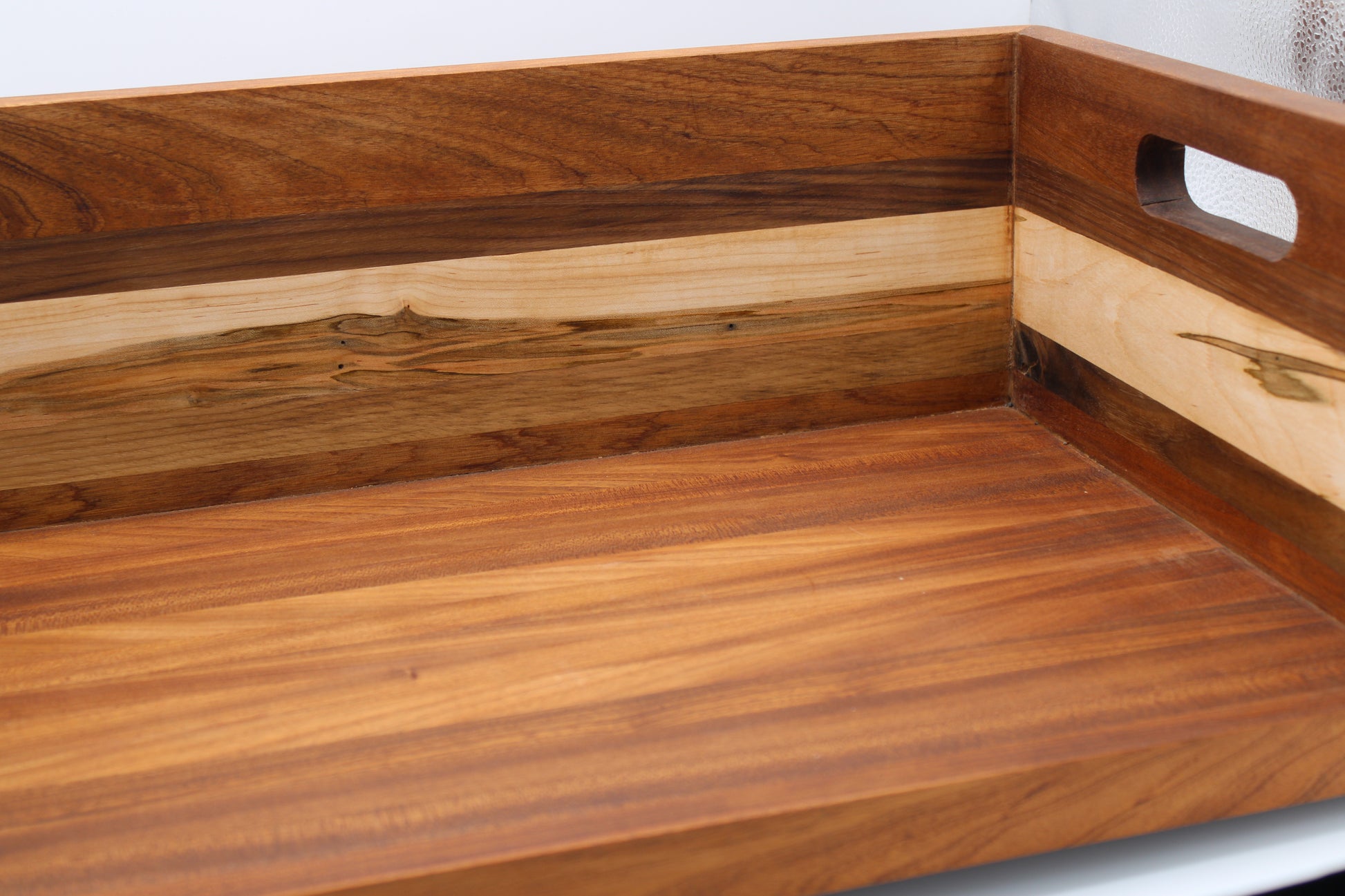 Close-up of a wooden serving tray with a warm medium-brown wood grain finish and a lighter natural wood inlay, featuring a cutout handle on the side.