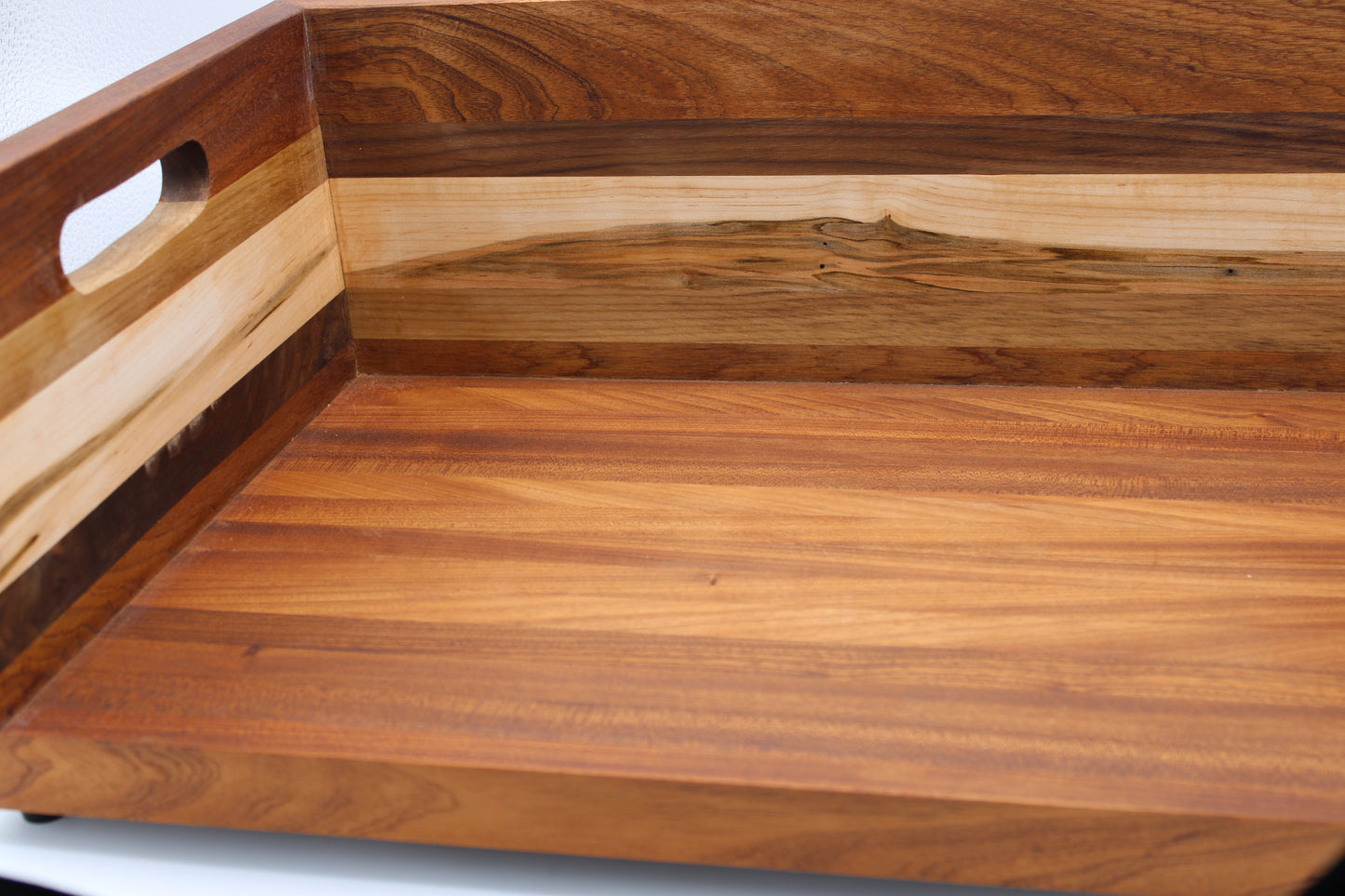 Close-up of a wooden serving tray or board with a cutout handle on the side, showing layered wood grain in warm brown and tan tones.