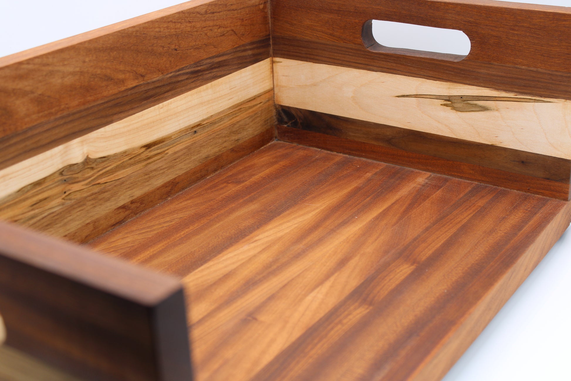 A close-up of a wooden serving tray with a handle cutout, showcasing a mix of dark and light wood grain panels.