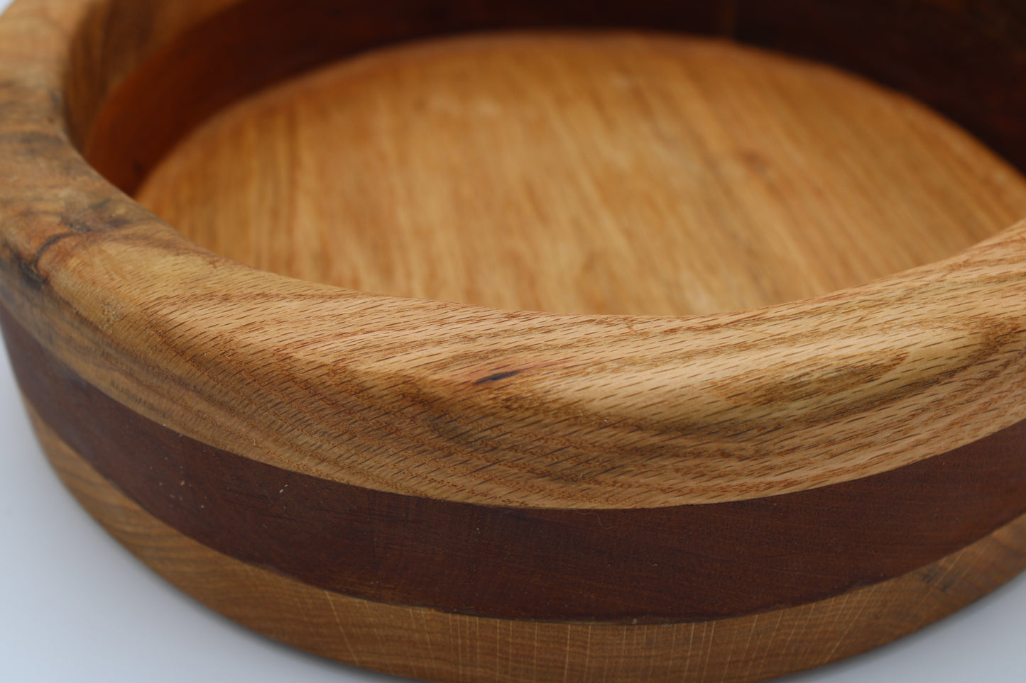 A close-up of a round wooden bowl or tray with a light tan wood body and a dark brown inlay band, shown on a white background.