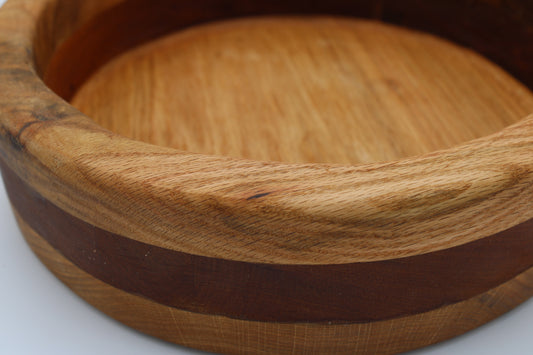 A close-up of a round wooden bowl or tray with a light tan wood body and a dark brown inlay band, shown on a white background.