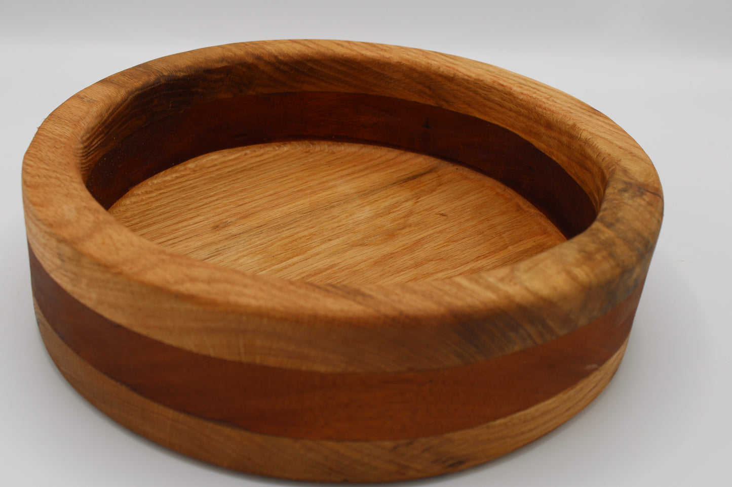 A round wooden bowl with a natural grain pattern and a darker brown inlay band, photographed on a neutral light gray background.