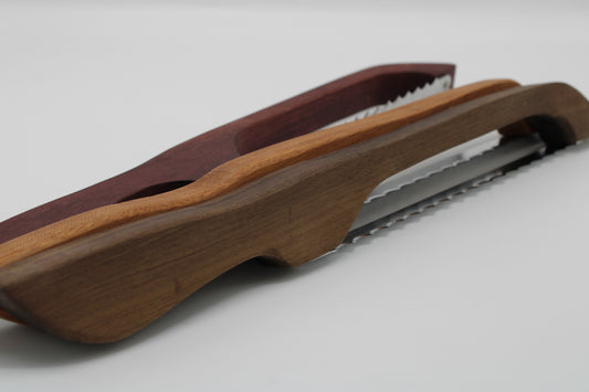 A close-up of a wooden folding saw with a dark reddish-brown handle and a lighter brown wood inlay, showing the serrated metal blade against a light gray background.