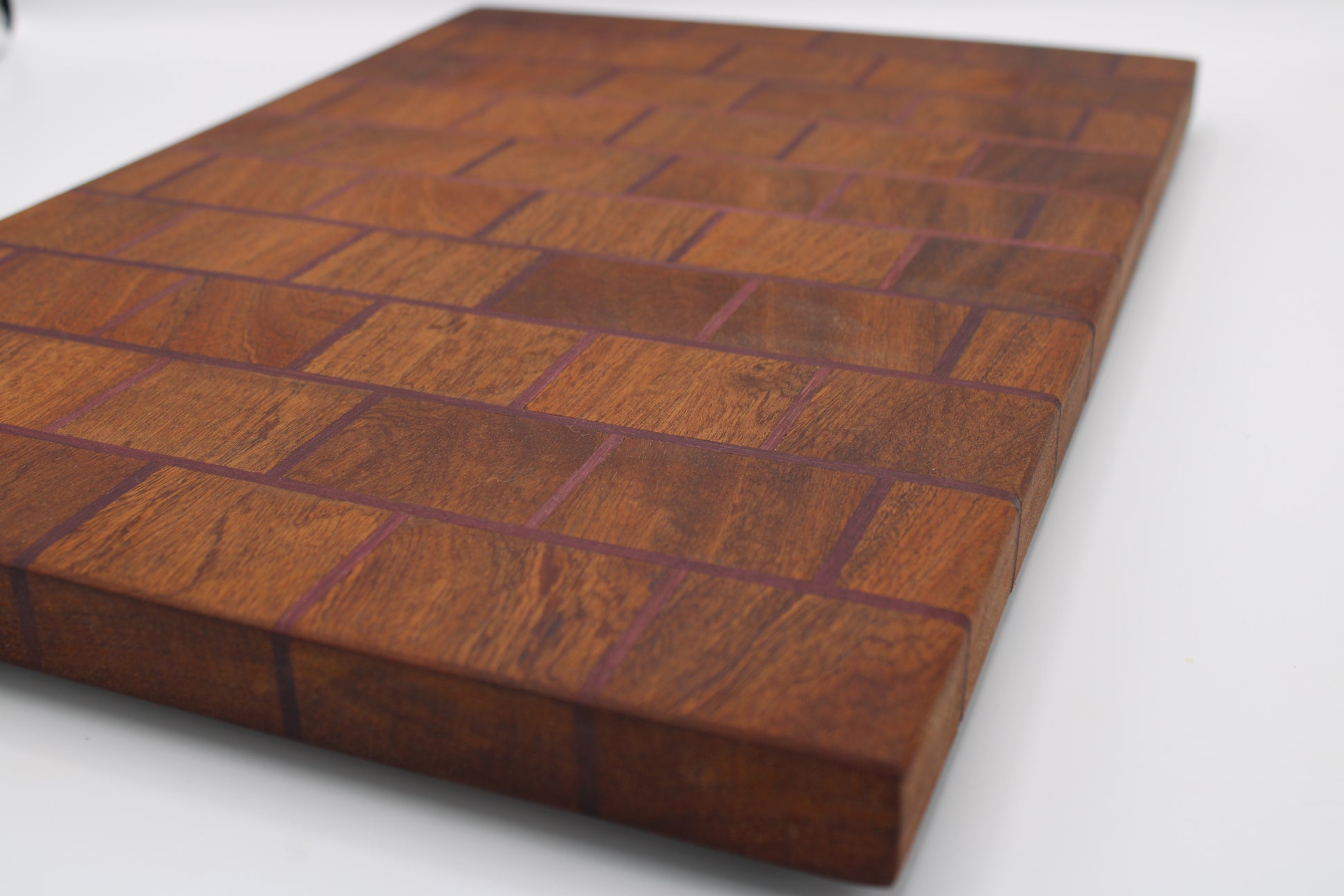 A rectangular wooden cutting board with a herringbone pattern made of alternating warm brown and reddish-brown wood blocks, shown on a plain white background.
