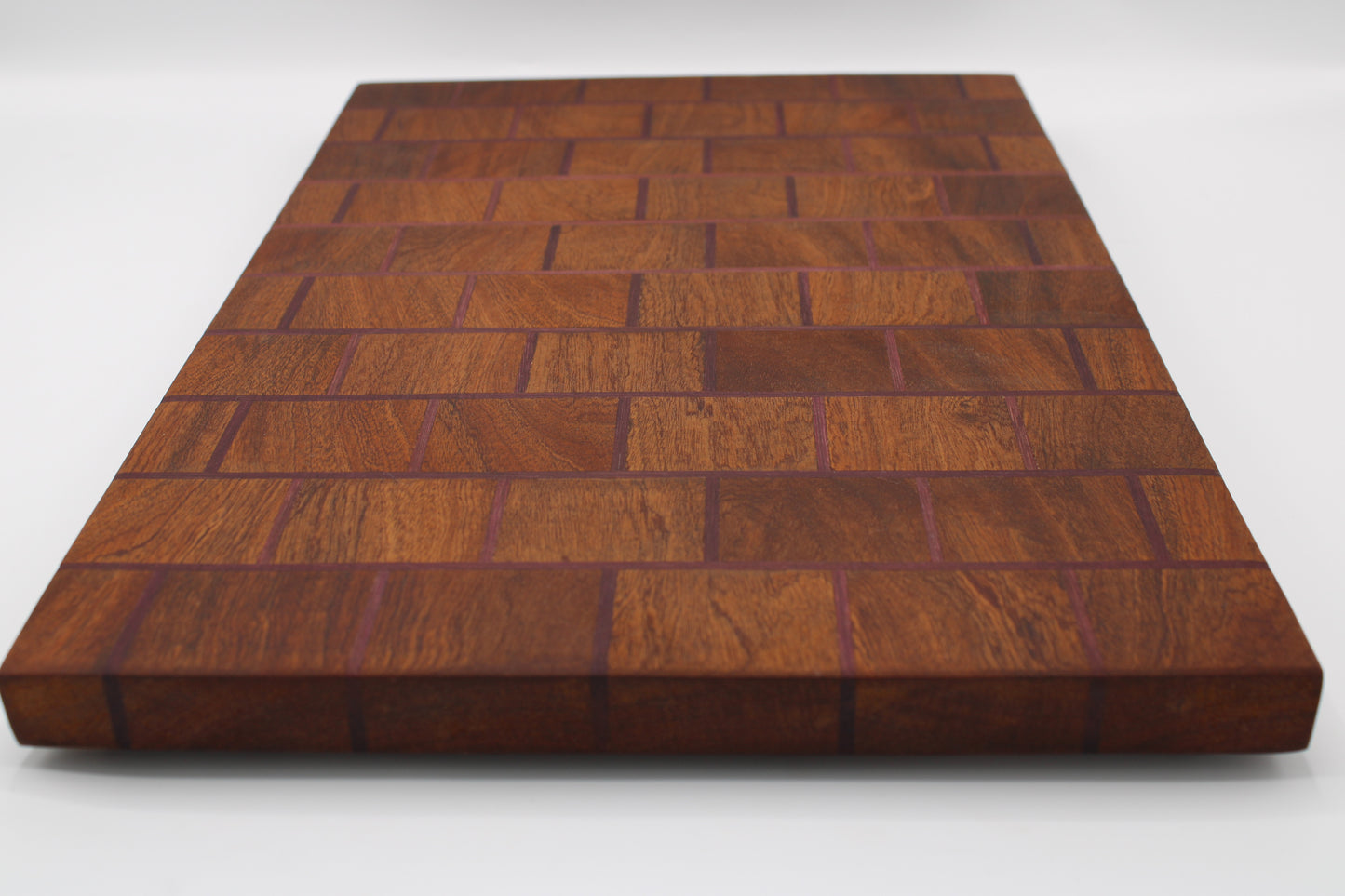 A rectangular wooden cutting board with a herringbone block pattern, made from dark reddish-brown wood pieces, shown on a white background.