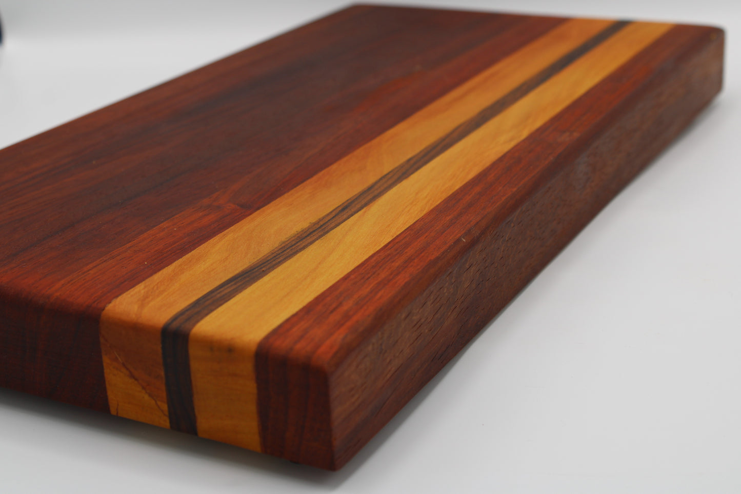 A rectangular wooden cutting board with a rich striped inlay design, featuring dark reddish-brown wood, golden-yellow wood, and thin black accents, photographed on a clean white background.