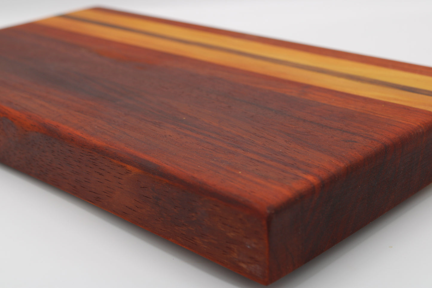 A close-up of a rectangular wooden board with a rich reddish-brown wood grain and two parallel light tan stripes near the top edge, photographed on a white background.