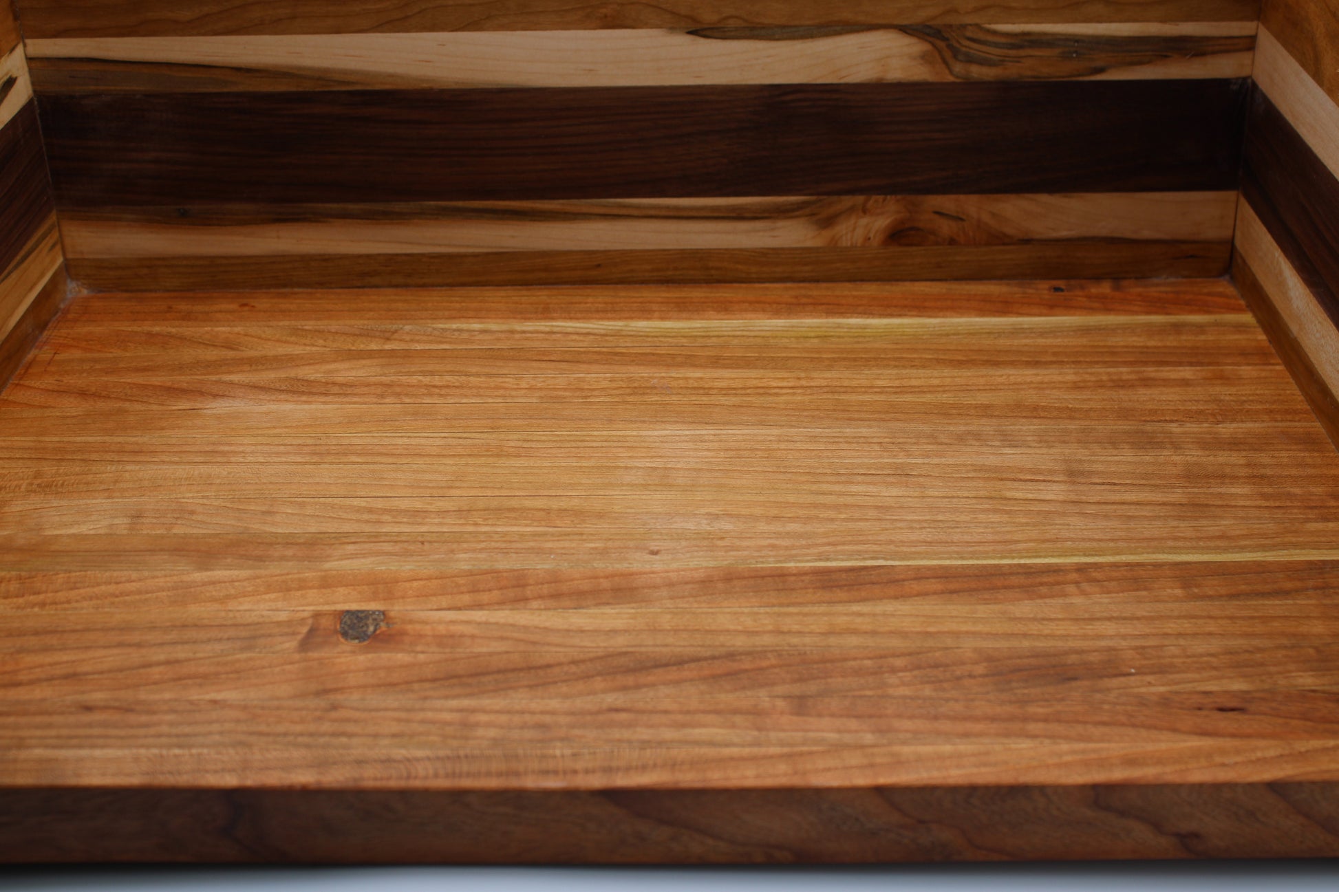 Close-up of a BBQ Chopping Box  made from layered wood strips, showing a warm medium-brown grain surface with darker brown bands along the top edge.