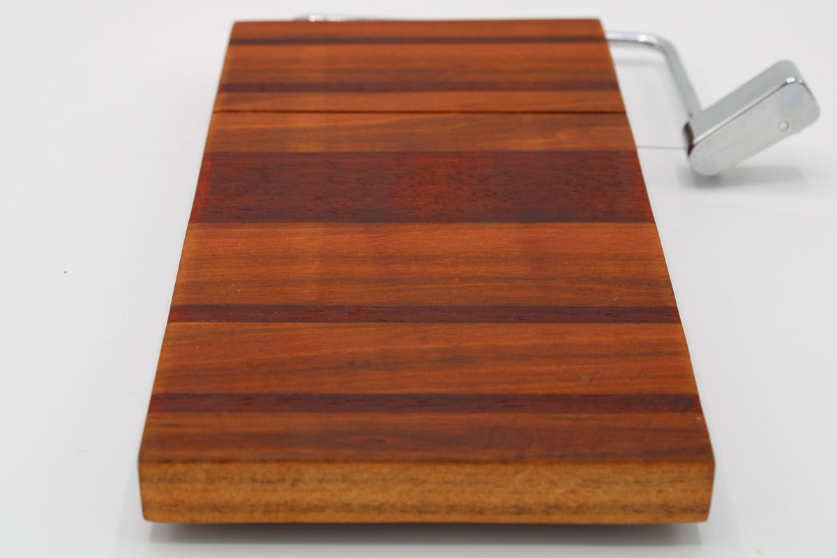 A rectangular wooden cheese board with alternating warm brown and reddish wood stripes, featuring a silver metal handle on the right side, shown on a plain white background.