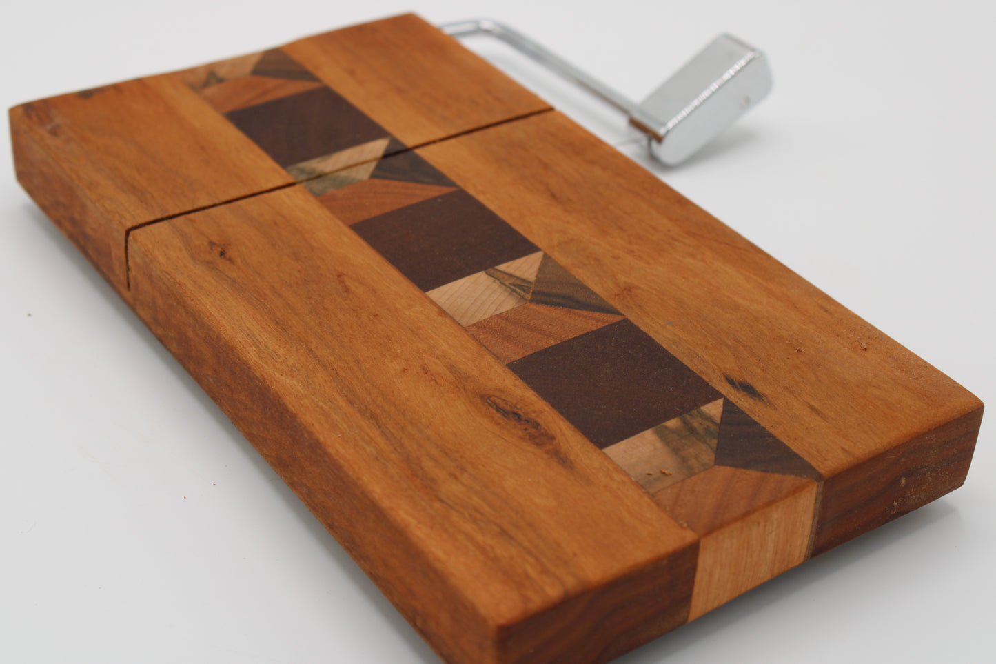 A wooden cheese board with a geometric inlay design and a silver metal handle, shown on a plain white background.